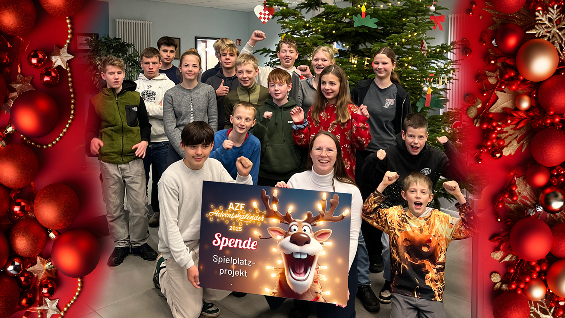 Viele Kinder stehen vor einem großen Tannenbaum in einer Schule und Jubeln in die Kamera, zwei Personen halten eine Spendentafel im Vordergrund.